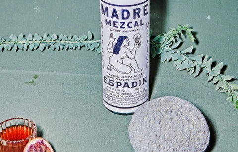 Mezcal bottle on green table beside a vine