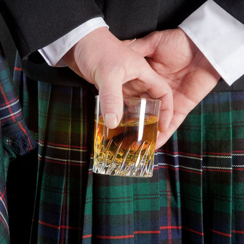 man holding a glass of whiskey wearing a traditional kilt
